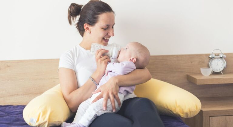 Mor giver baby sutteflaske og bruger en ammepude
