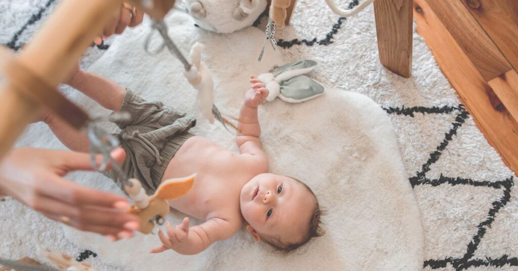Baby ligger på et tæppe og kigger på en baby uro